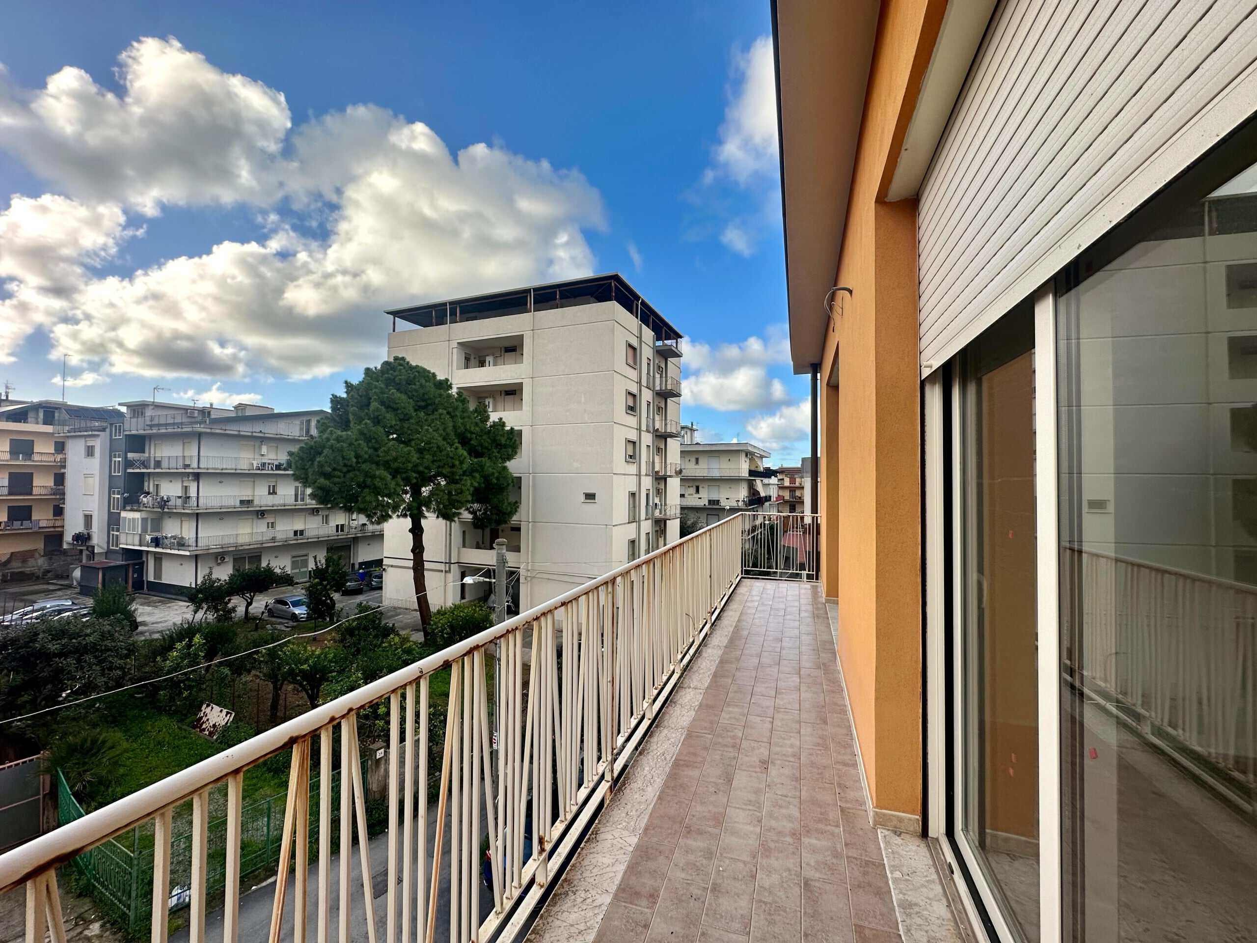 Spazio esterno di un appartamento con terrazza, vista su edifici residenziali e alberi, cielo sereno con nuvole bianche, ambiente luminoso e accogliente, ideale per relax all'aperto.
