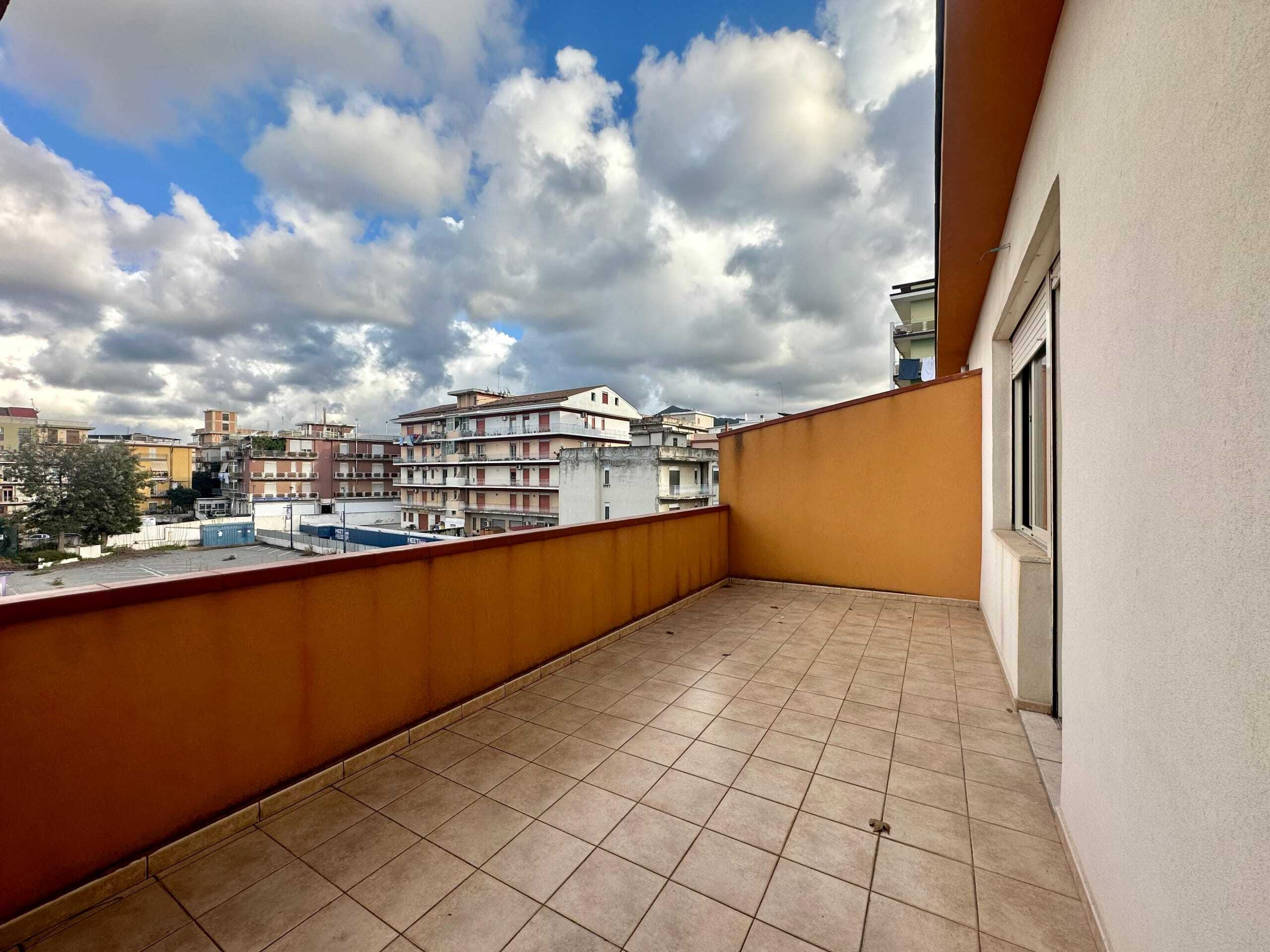 Balcone spazioso con vista sugli edifici cittadini, pavimentato in gres e pareti di colore arancione, ideale per relax e vivacità urbana.