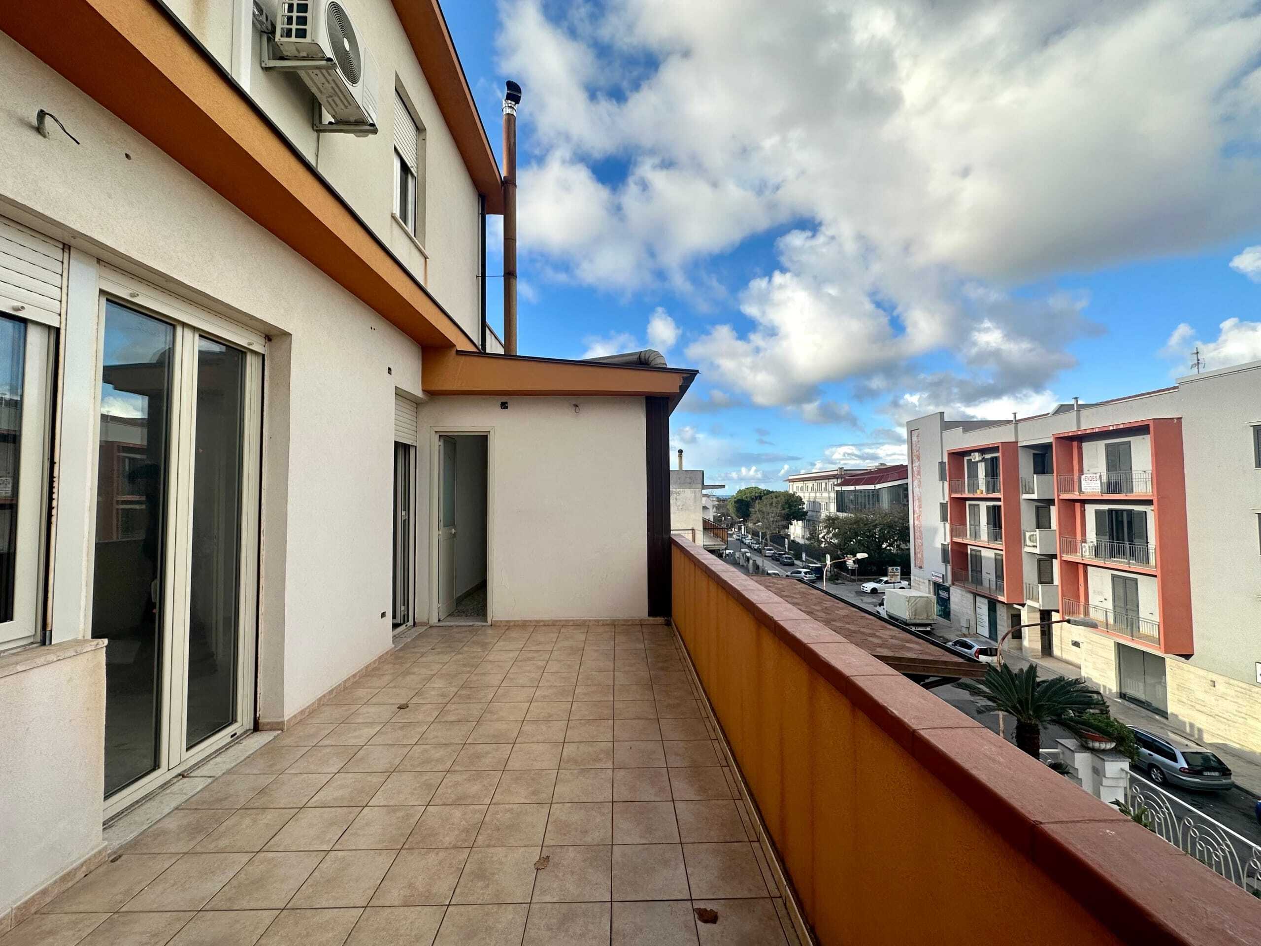 Balcone spazioso con vista sulla città, pavimentazione in ceramica e muro di recinzione arancione, ideale per relax e vita all'aperto in zona residenziale.