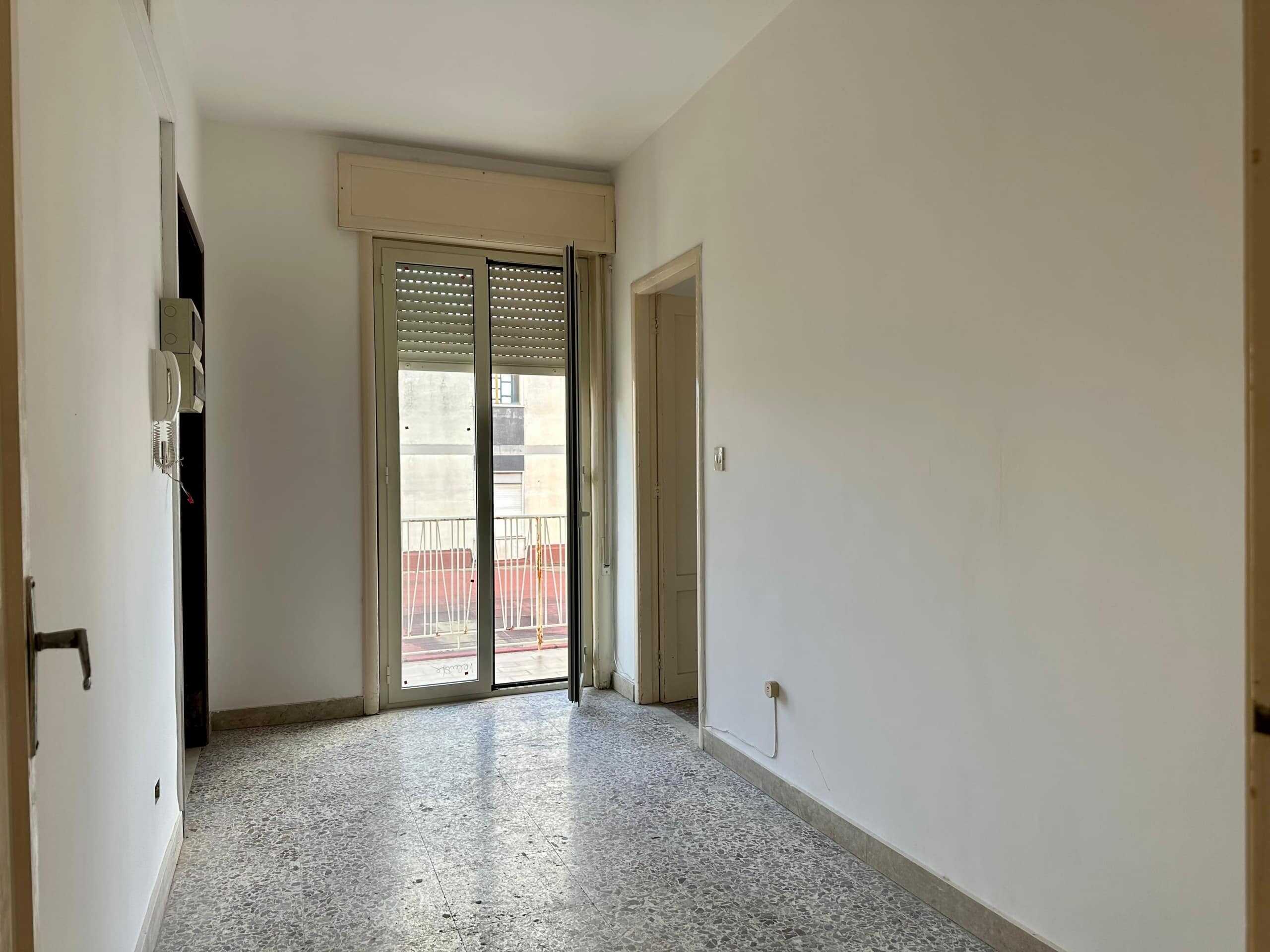 Appartamento con balcone e porte-finestre in zona residenziale, luminoso e spazioso, ideale per affitti turistici o abitativi, con vista su edifici circostanti, in stile semplice e funzionale.