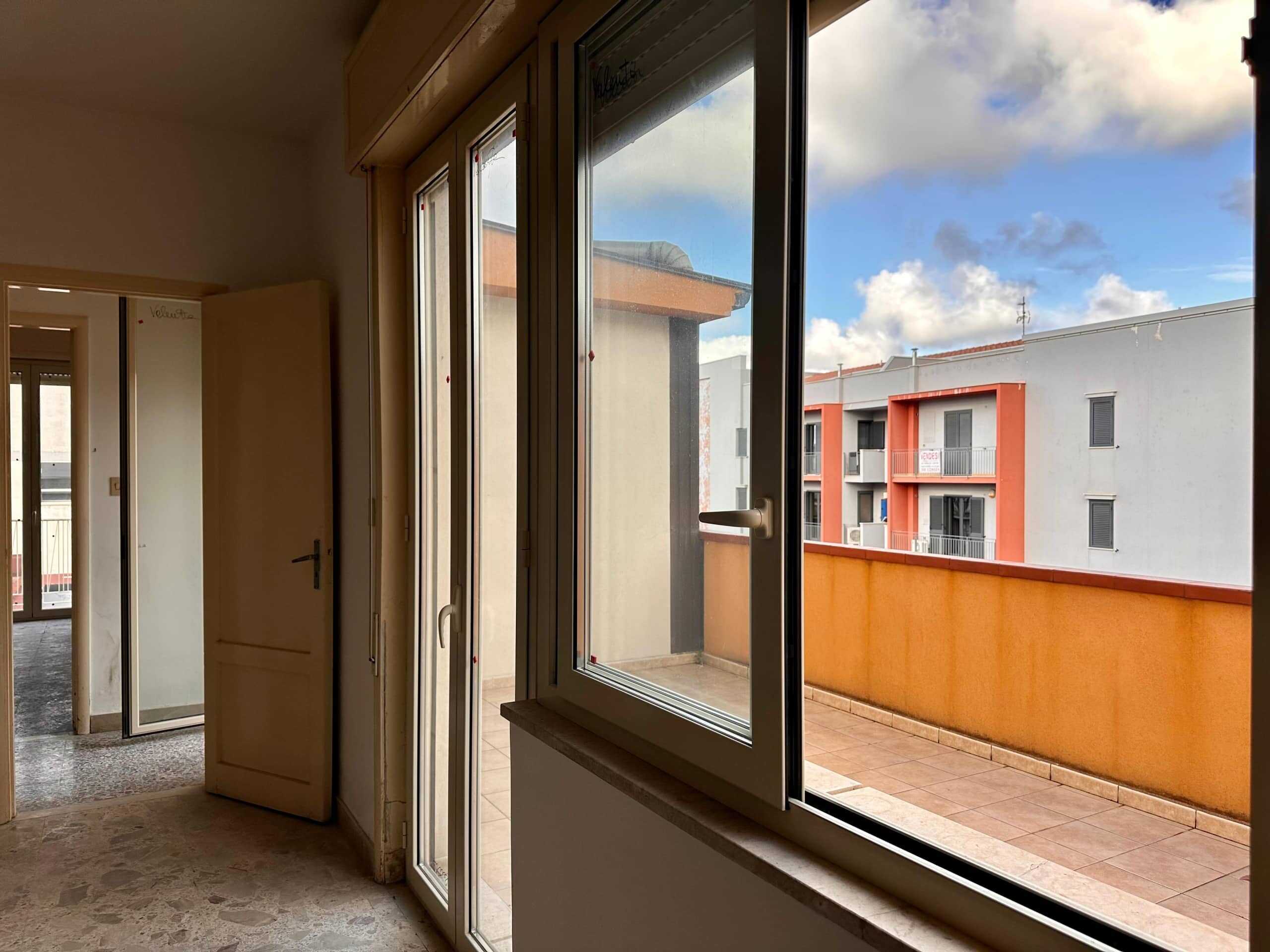 Balcone di appartamento con finestre a doppio vetro e vista su edificio residenziale colorato, spazio esterno soleggiato e accessibile, ideale per rilassarsi o pranzare all'aperto.