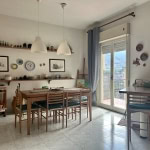 Elegante sala da pranzo con tavolo in legno, grande finestra con vista sulla città e decorazioni artistiche alle pareti, in uno stile accogliente e luminoso, ideale per abitazioni di design.