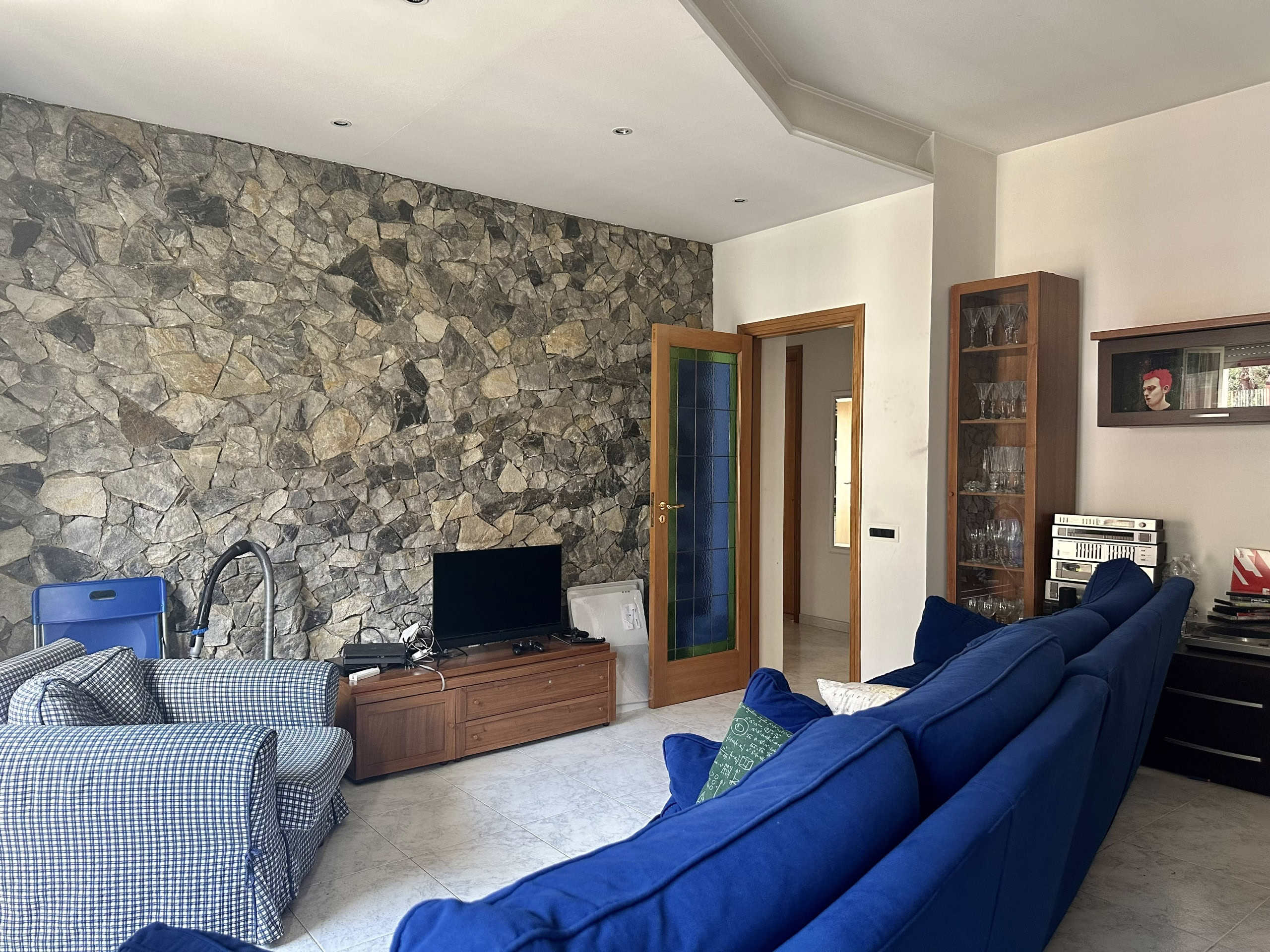 Parete in pietra naturale in soggiorno, arredi in stile classico moderno, divani blu, mobile TV, lampada, decorazioni, ambiente accogliente e elegante, casa NextCasa in Italia.