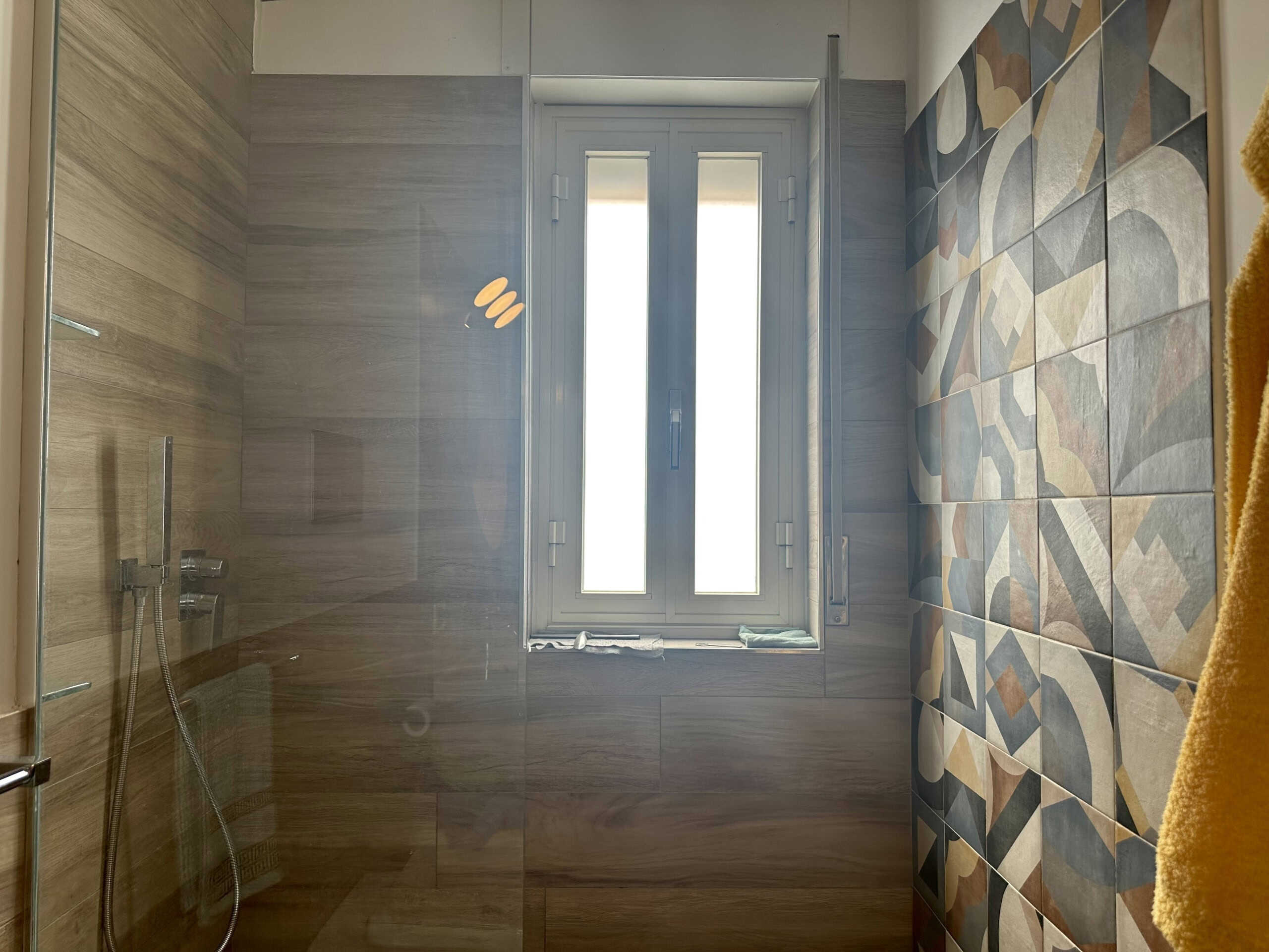 Pioggia di luce naturale su bagno moderno con pareti in legno e piastrelle decorative geometriche. Atmosfera calda e accogliente, ideale per momenti di relax e benessere.