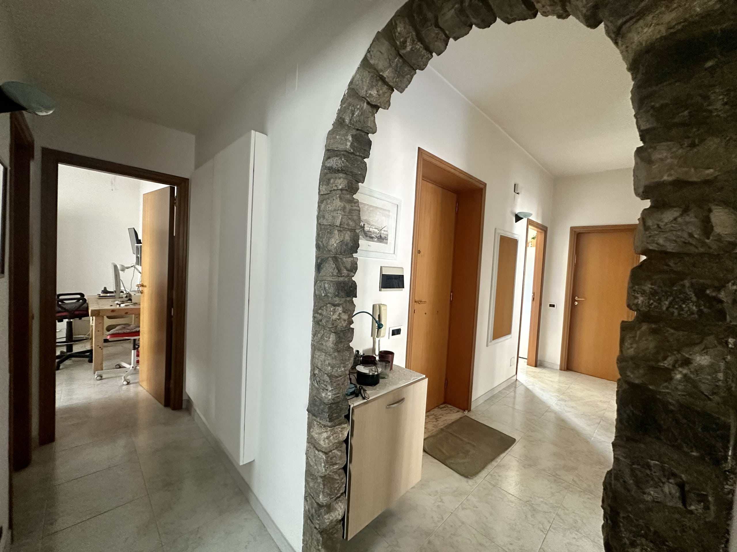 Ingresso di casa con muro in pietra a vista, porte in legno e spaziosa hall con arredamento moderno e ambienti luminosi.
