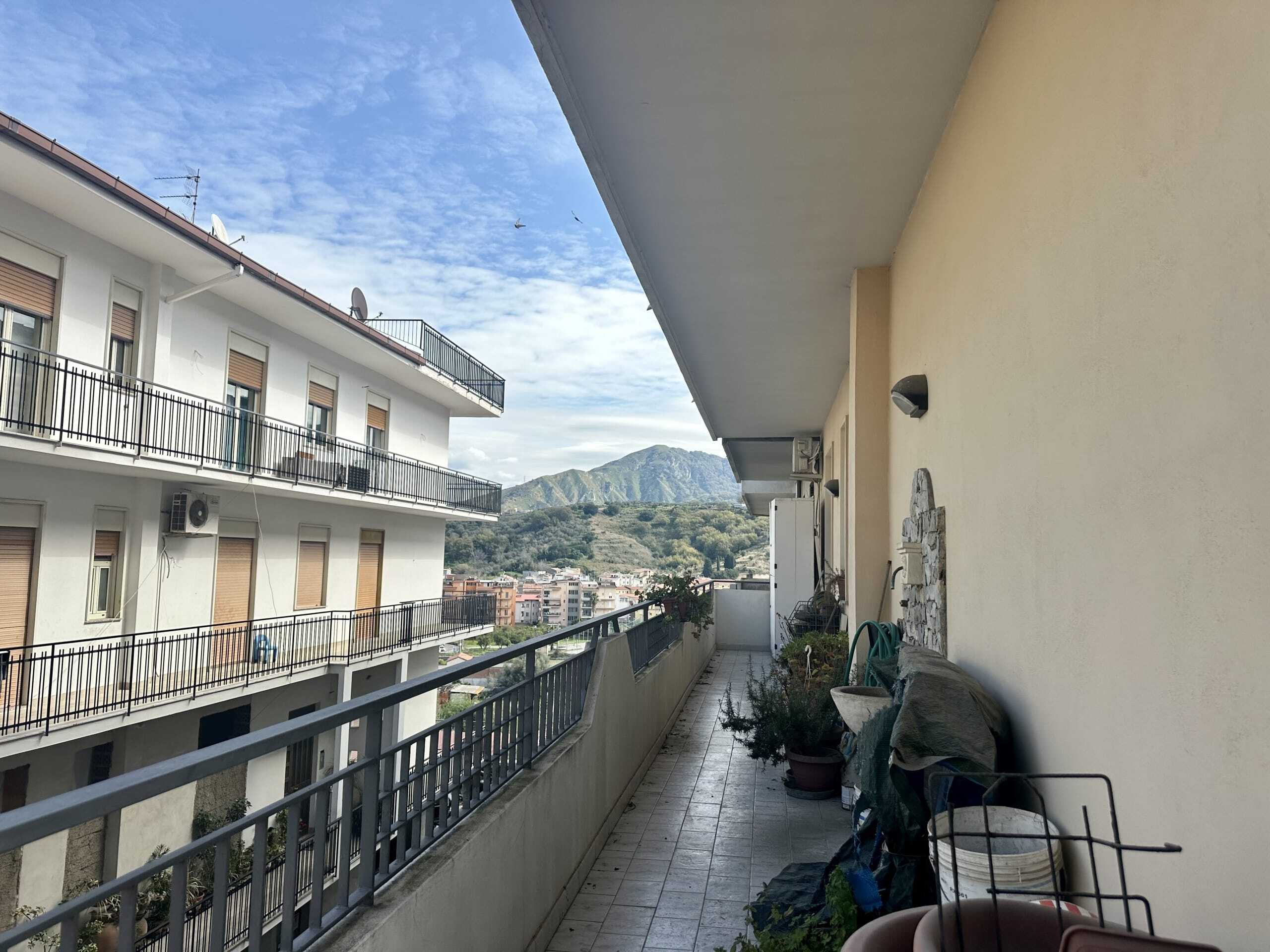 Balcone spazioso con vista sulle montagne e sulla città, ideale per relax e attività all'aperto, dotato di piante e arredi esterni in un edificio residenziale a più piani.