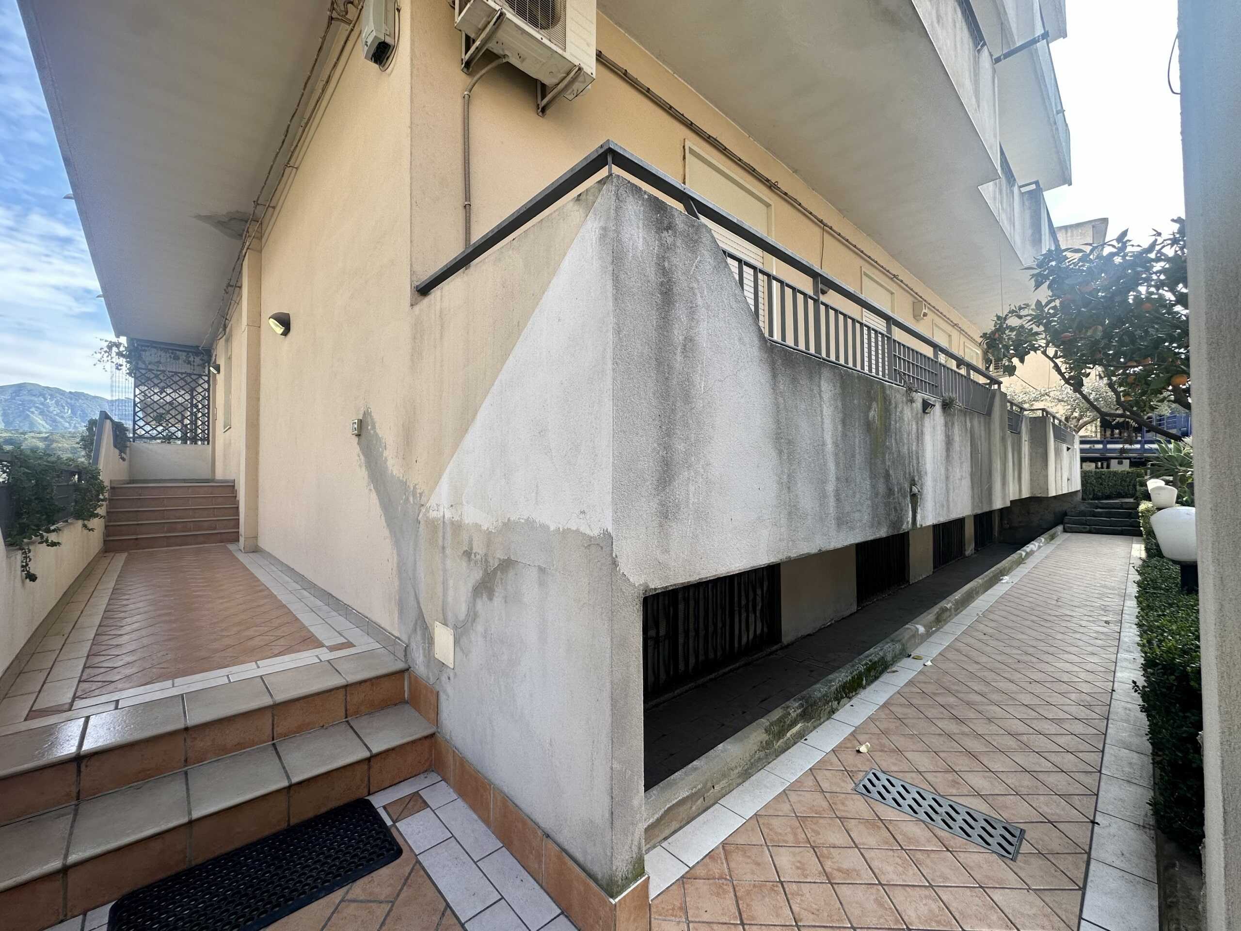 Segnale di accesso al piano superiore con scale esterne e balcone in pietra e ferro battuto, all'esterno di un appartamento in zona urbana.
