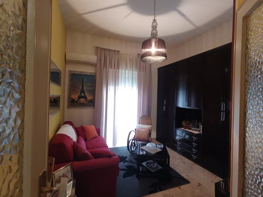 Accogliente zona living con divano rosso, pareti decorate, grande armadio nero e finestra con tende leggere, arredamento elegante, ideale per case spaziose e moderne.