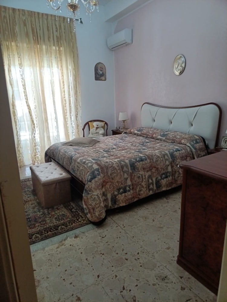 Letto matrimoniale con testiera imbottita, arredo camera da letto classico, calde tende di pizzo, decorazioni vintage, stile casa elegante.