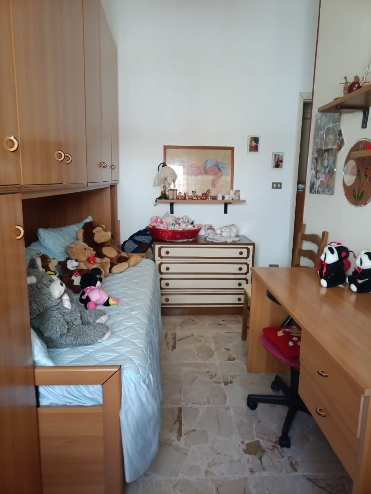 Letto con divano letto, molti peluche e armadio in legno chiaro, decorazioni affiancano a uno spazio cameretta accogliente e ordinata.