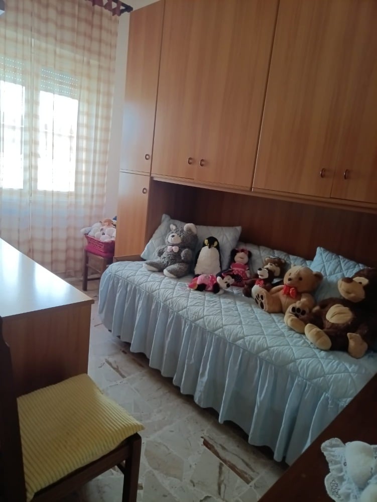 Comodino con ripiani e armadio a muro in legno in una camera dei bambini con cuscini e bambole assortite, luce naturale, ambiente accogliente e ordinato.