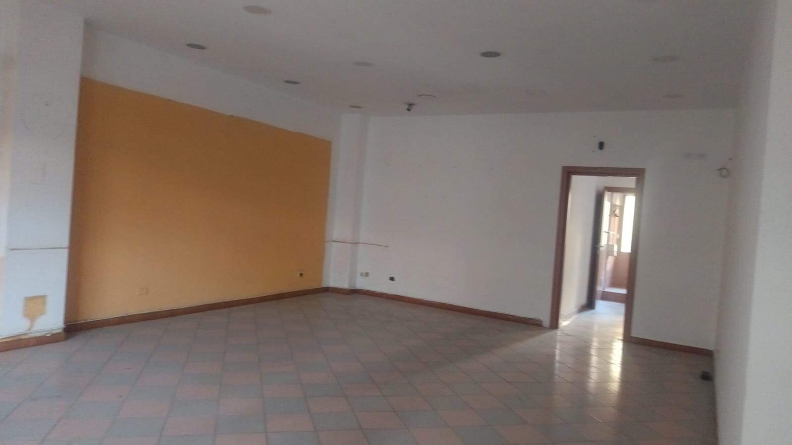 Spazio commerciale o ufficio vuoto con parete arancione e pavimento in piastrelle colorate. Entrata con porta e finestra che lascia entrare luce naturale, ideale per affitto o vendita immobili.