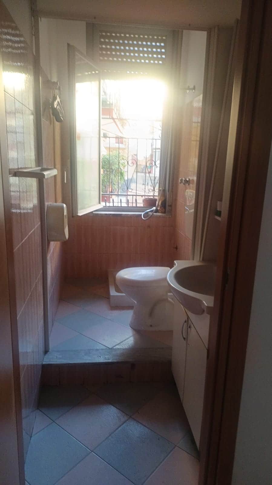 Balcone con finestra e vista sulla città, illuminato dal sole mattutino, in un appartamento in stile tradizionale italiano.