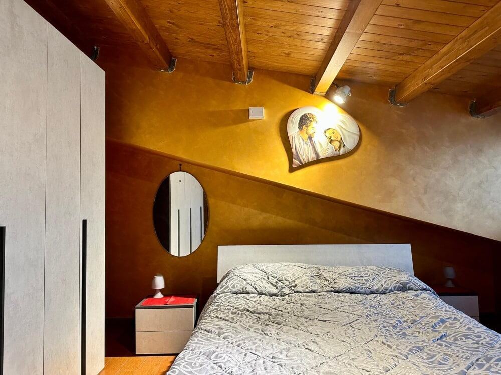 Letto matrimoniale in stile moderno con pareti di tonalità calda, sotto un soffitto in legno a vista, in una camera da letto di design NextCasa.