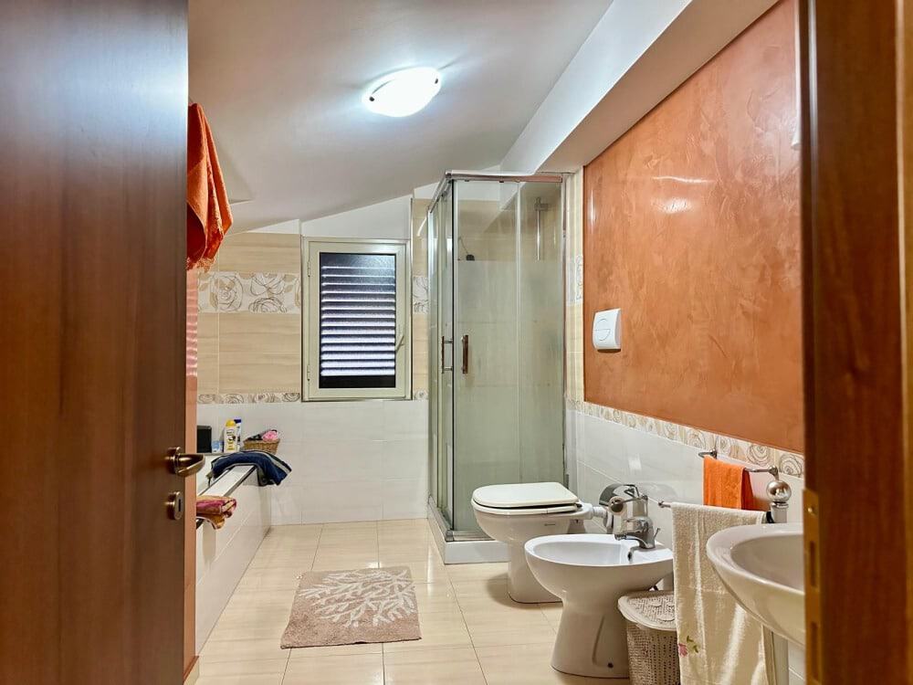 Grande bagno moderno con box doccia, bidet, lavabo, finestra, pareti colorate, accessori bagno, arredamento funzionale, spazio confortevole, piastrelle chiare, decorazione elegante, ristrutturazione casa, NextCasa, immobili in vendita e affitto.