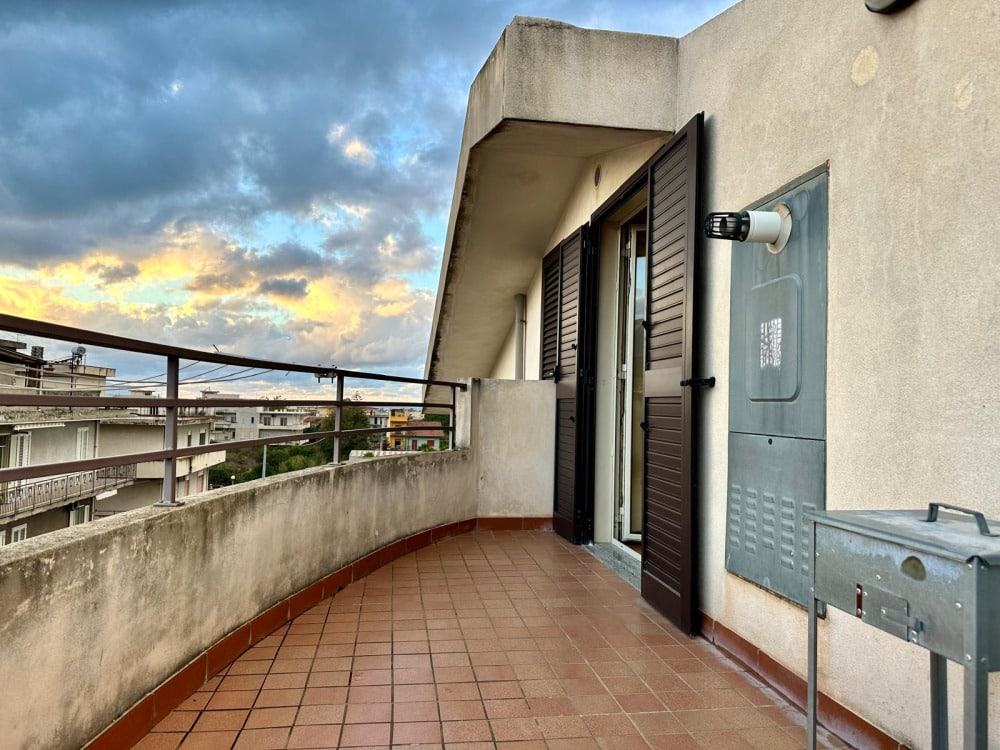 Balcone panoramico di un appartamento con vista sulla città, con parapetto in metallo, pavimentazione in piastrelle e pannelli di persiana in legno, ideale per appartamenti in vendita o affitto.