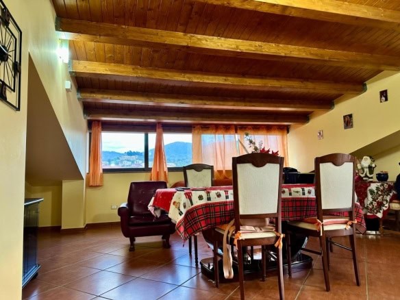 Azienda immobiliare NextCasa, appartamento in affitto con soggiorno con travi in legno, arredamento rustico, vista panoramica sulle colline dal grande finestrone. Condominio vicino ai servizi.