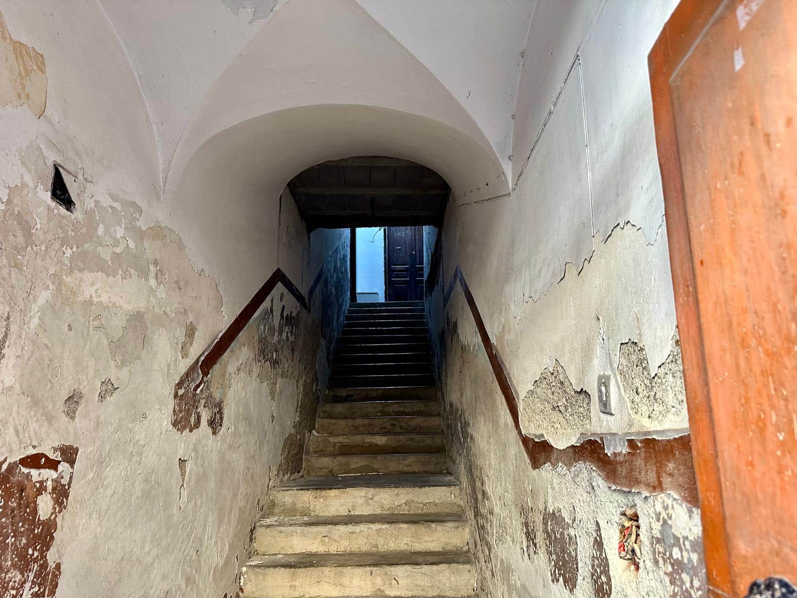 Vecchia scala di pietra in affaccio su muro con pareti con vernice scrostata e deteriorata, ingresso di un edificio storico o rustico, ambiente interno decadente e autentico, in stile vintage.