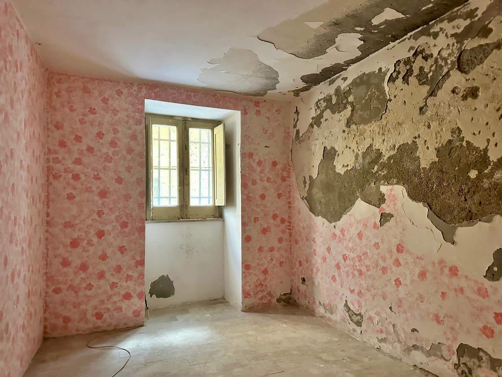Vecchio appartamento in ristrutturazione con pareti danneggiate e decorazioni in fase di completamento, ambiente luminoso con finestra a vetri.