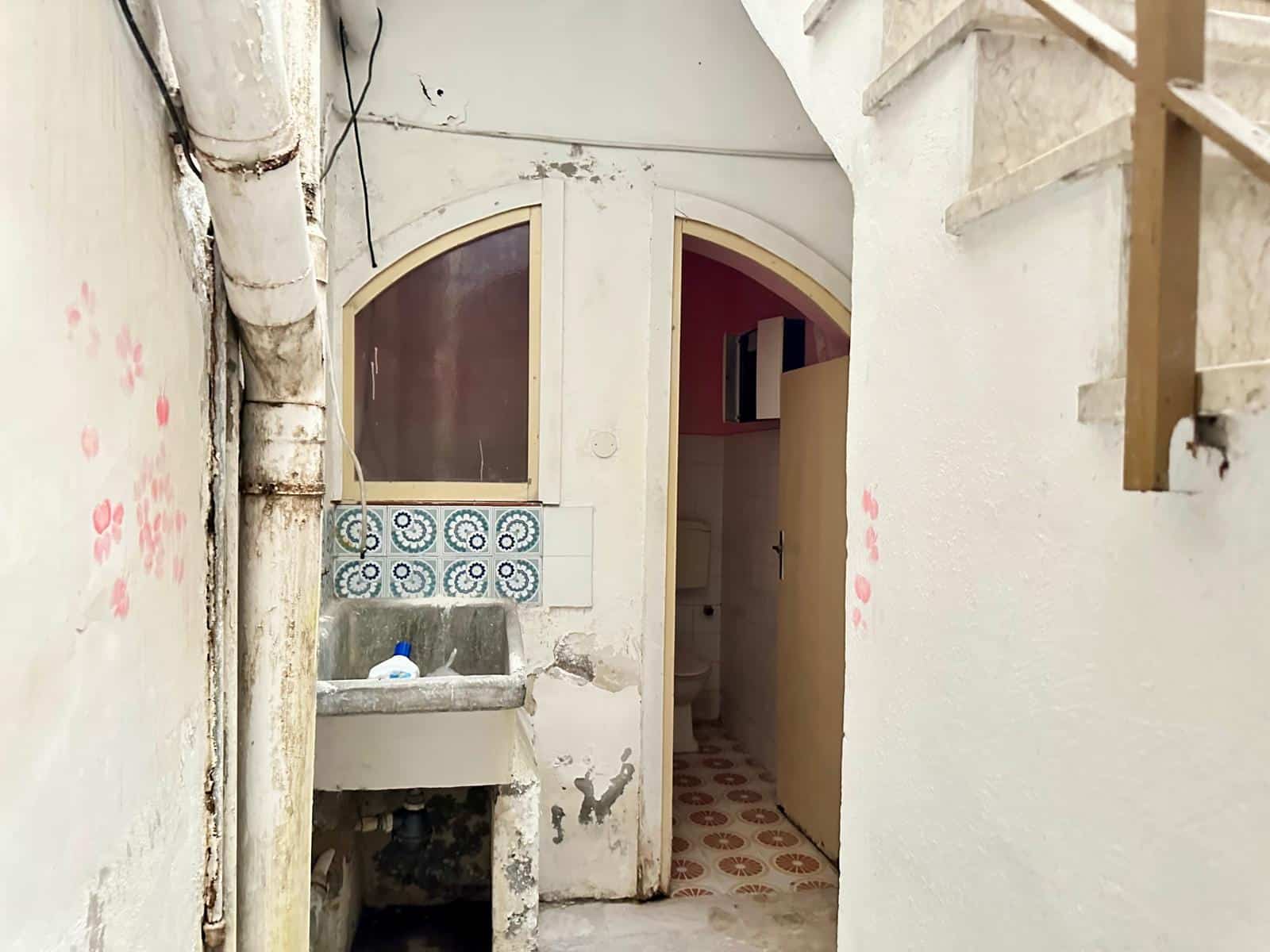 Lavabo in condizioni di ristrutturazione con piastrelle decorative e pareti bianche, spazio riservato a servizi igienici, ambiente di una casa in fase di ristrutturazione, vicino a scale in legno.