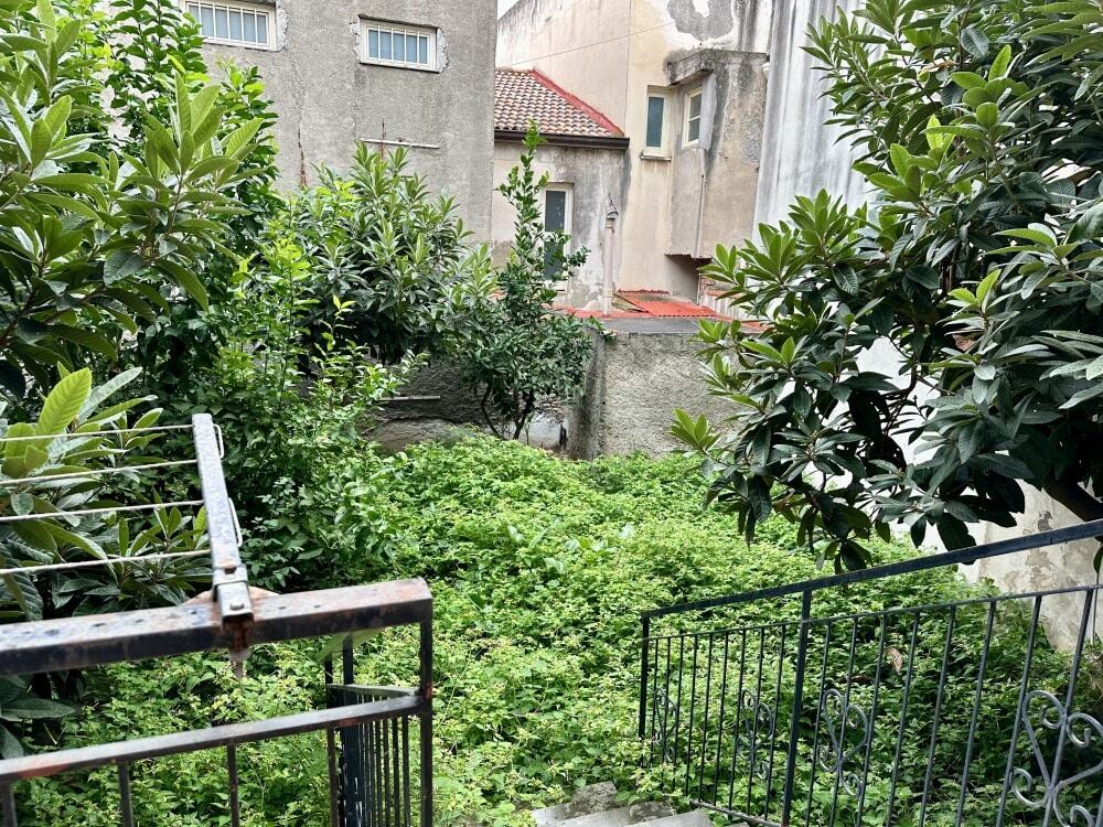 Giardino privato con piante rigogliose e alberi in un cortile interno di una casa urbana, ambiente tranquillo e verdeggiante, ideale per relax e svago all'aperto.