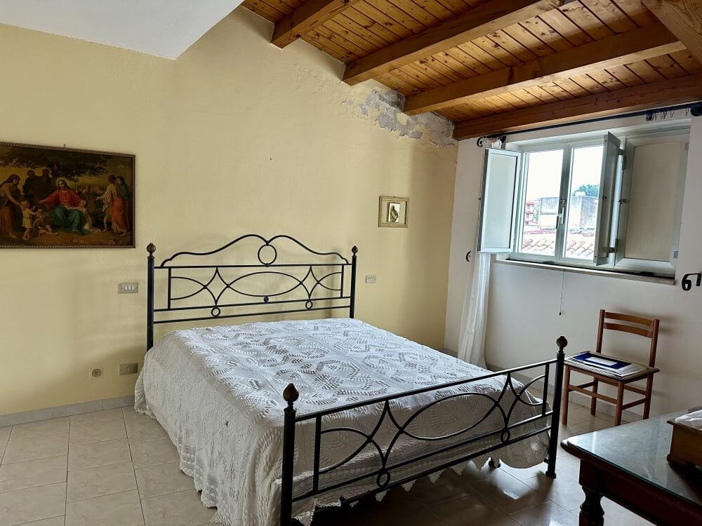 Letto matrimoniale con testiera in ferro battuto in una camera luminosa e accogliente con soffitto in legno e finestra che offre vista sulla città, perfetta per affitti di breve e lungo termine.