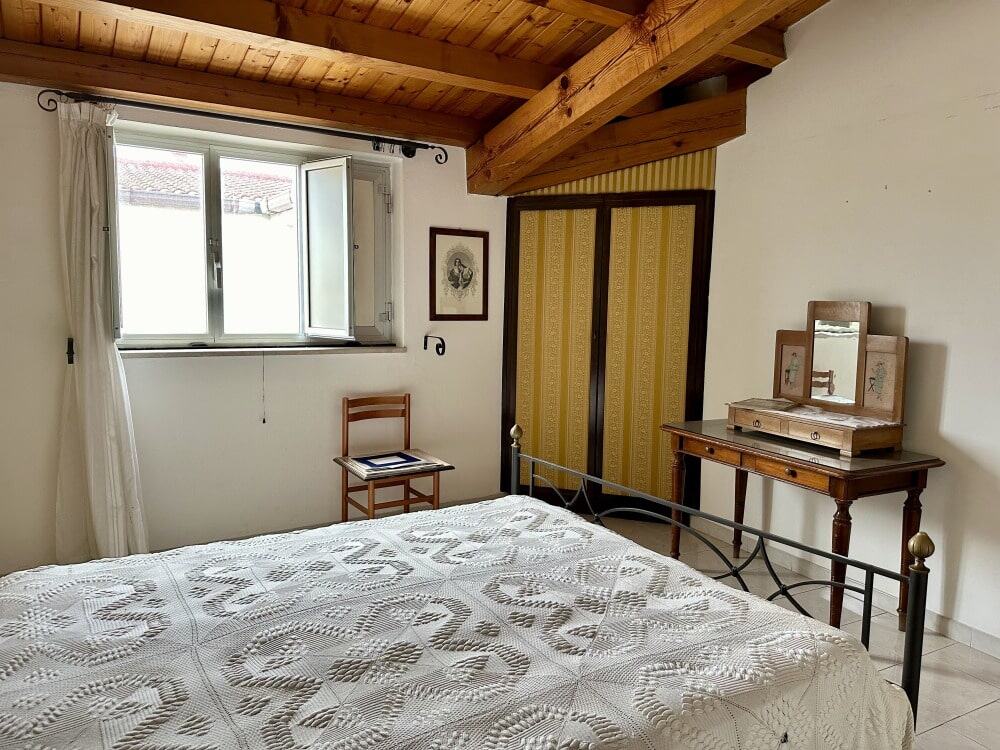Balcone di camera da letto con finestra aperta, arredo classico, letto in ferro battuto, scrivania in legno, decorazioni vintage, tetto in legno a vista, stile rustico.