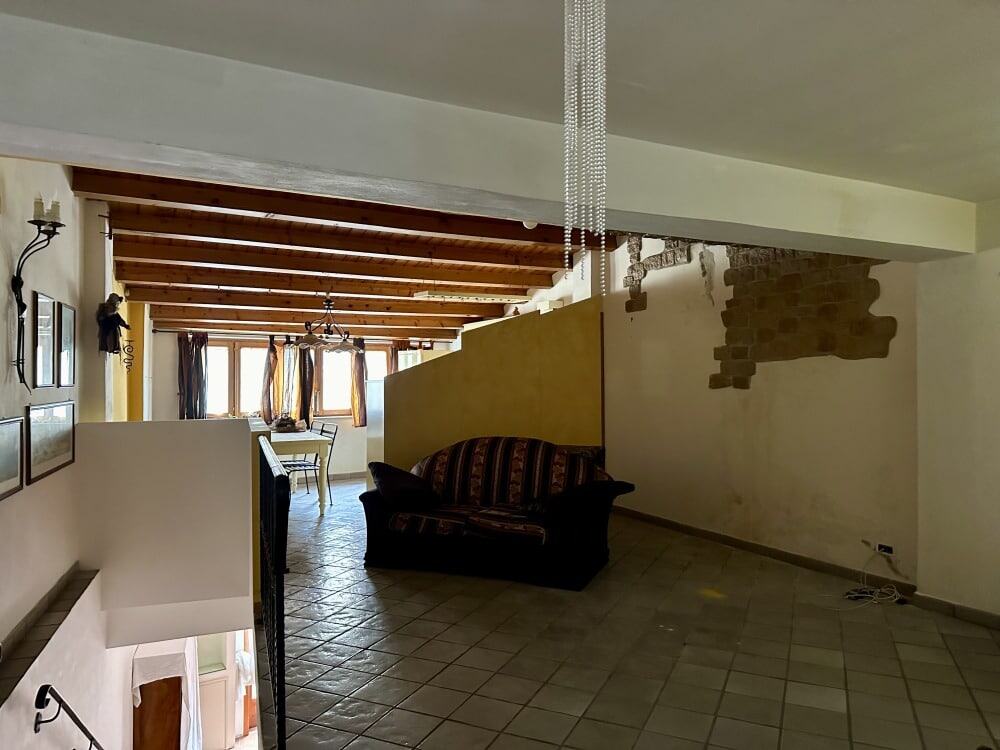 Ampio soggiorno con soffitto a travi in legno, pareti in stile rustico con mattoni a vista, zona living con divano e zona pranzo luminoso via finestre.