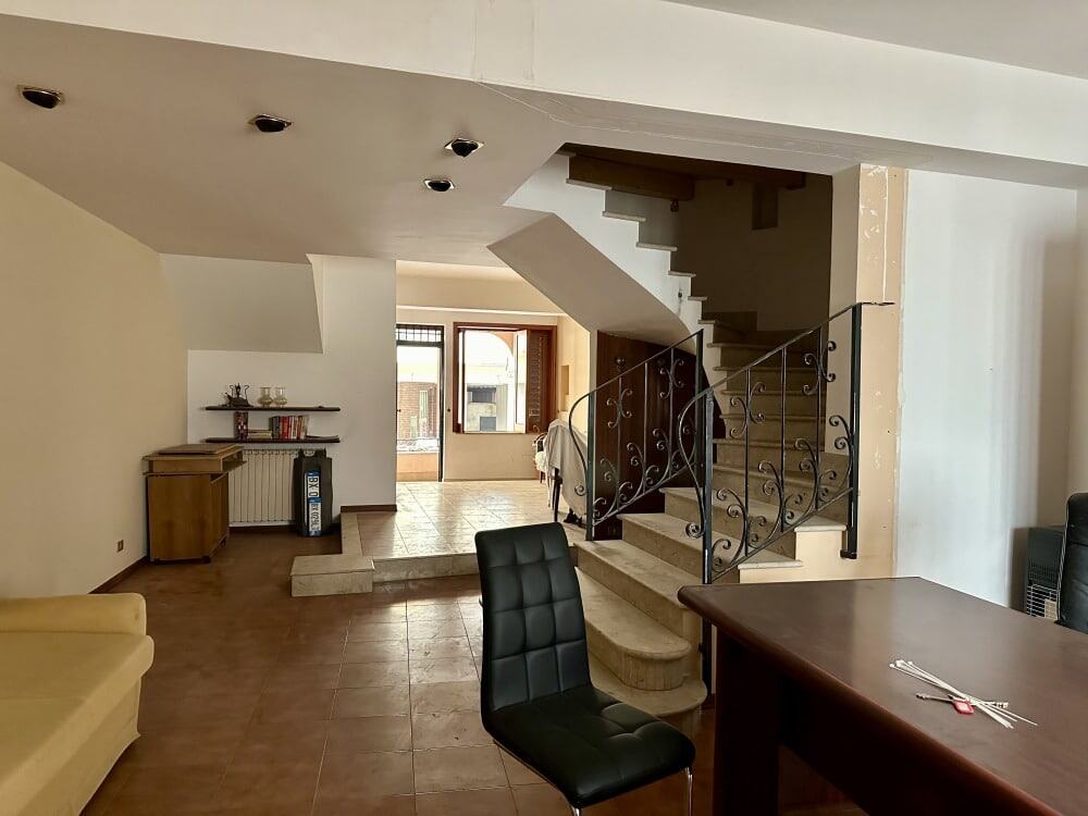 Ampia zona giorno con scala in legno, soggiorno e zona pranzo, spazio luminoso con grandi finestre, arredamento moderno e funzionale, ideale per abitazioni residenziali di qualità.