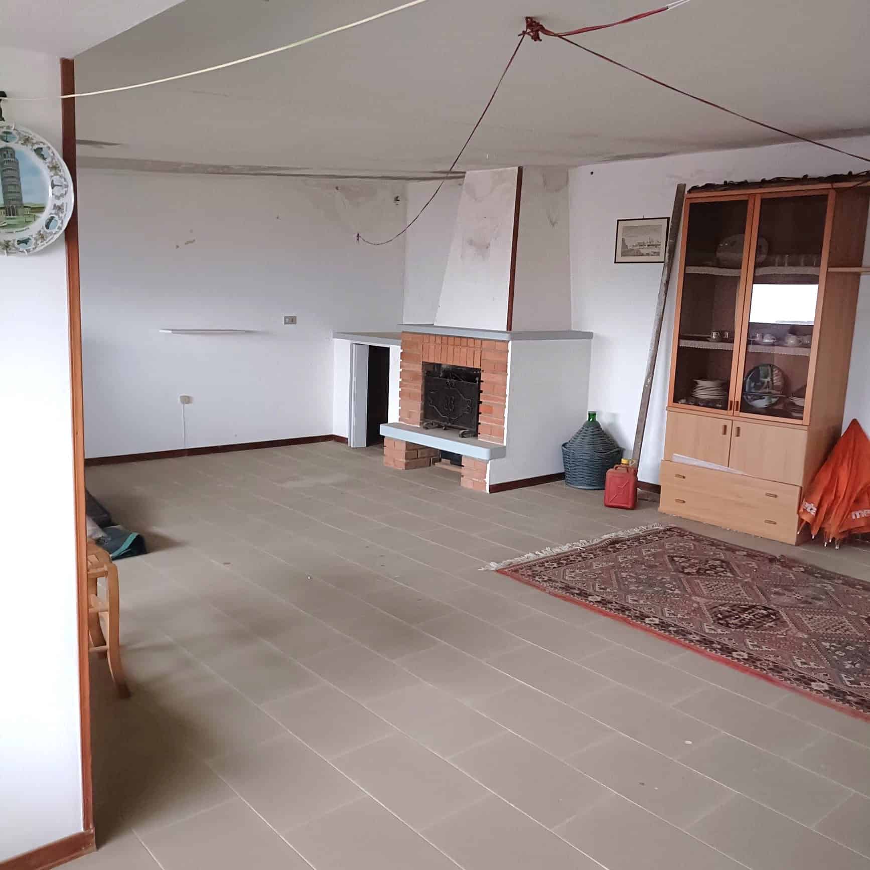 Pavimento in gres porcellanato beige, soggiorno con camino in mattoni e mobili in legno, ambiente luminoso e spazioso, ideale per ristrutturazione casa e arredo moderno.