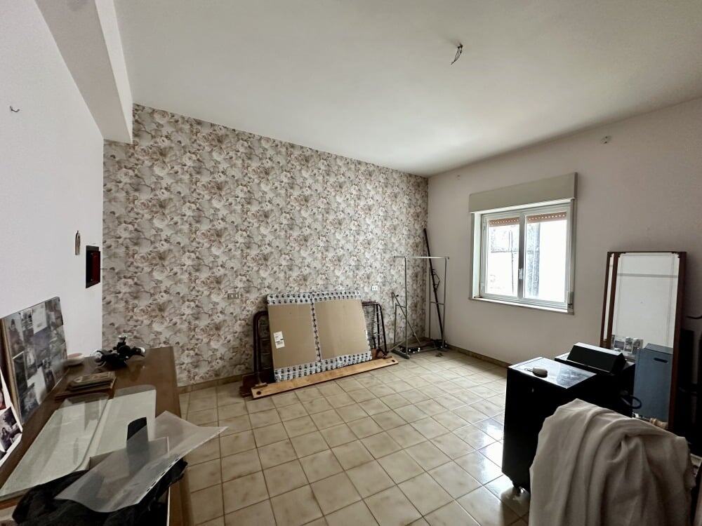 Stanza di casa in fase di ristrutturazione con parete decorativa, finestra luminosa e pavimento in ceramica, ideale per arredamento e trasformazioni immobiliari.