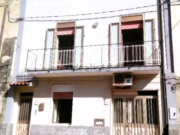 Immobile residenziale a tre piani con balcone, facciata bianca, finestre con grate e aria condizionata, situato in zona urbana, ideale per investimenti immobiliari.