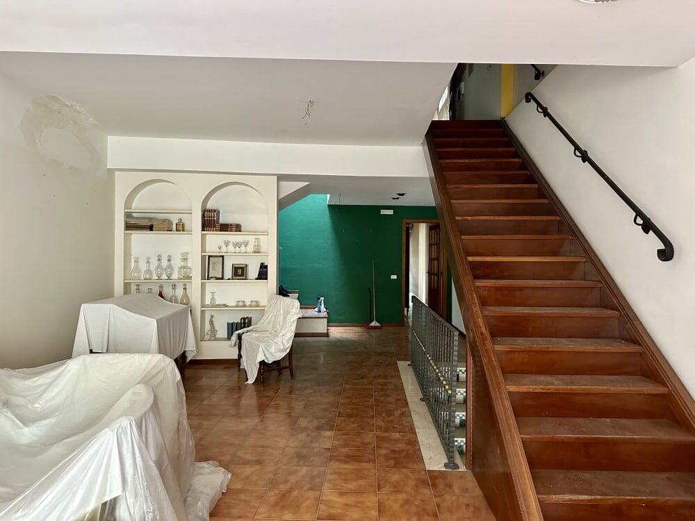 Scala in legno massello e lussuoso arredamento in soggiorno con parete verde. Ambiente residenziale elegante e accogliente, pronta per essere ristrutturata e personalizzata.
