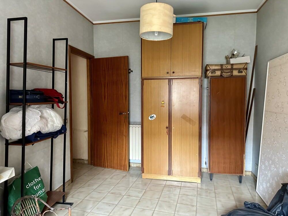 Armadio in legno, spazio di stoccaggio in una stanza con pareti grigie e pavimento in piastrelle beige, con scaffale nero, valigia e vario mobilio, ambiente abitativo domestico.