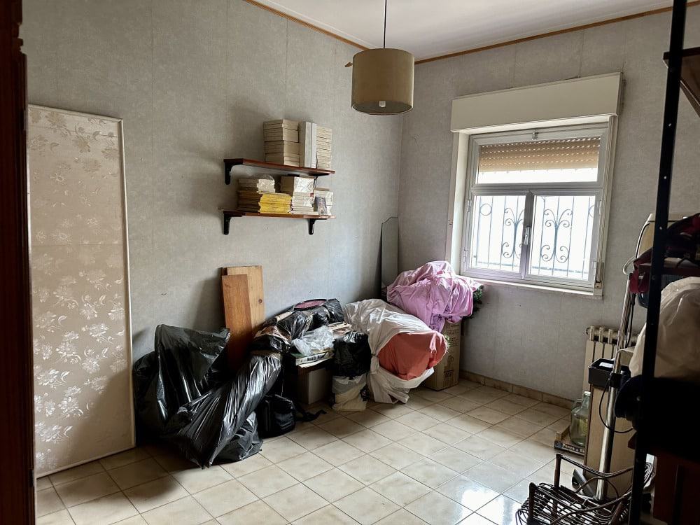 Vestito e camera trascurati in stanza con finestra con grate, arredamento minimal, organizzato con ripiani e scatole di cartone.