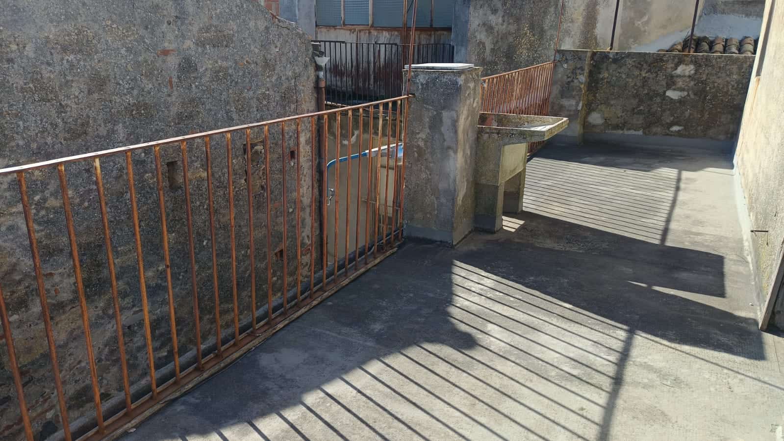 Fila di ferro battuto rossa su balcone con vista sul muro in pietra, spazio esterno con lavabo in pietra e parapetto in ferro, in un contesto residenziale storico, illuminato dal sole, atmosfera urbana e rustica.