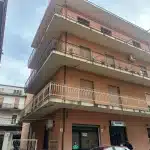 Villetta moderna con balconi in ferro battuto, edificio residenziale a tre piani, facciata in mattoni color terra cotta, aria condizionata e spazi esterni ben curati, zona urbana.