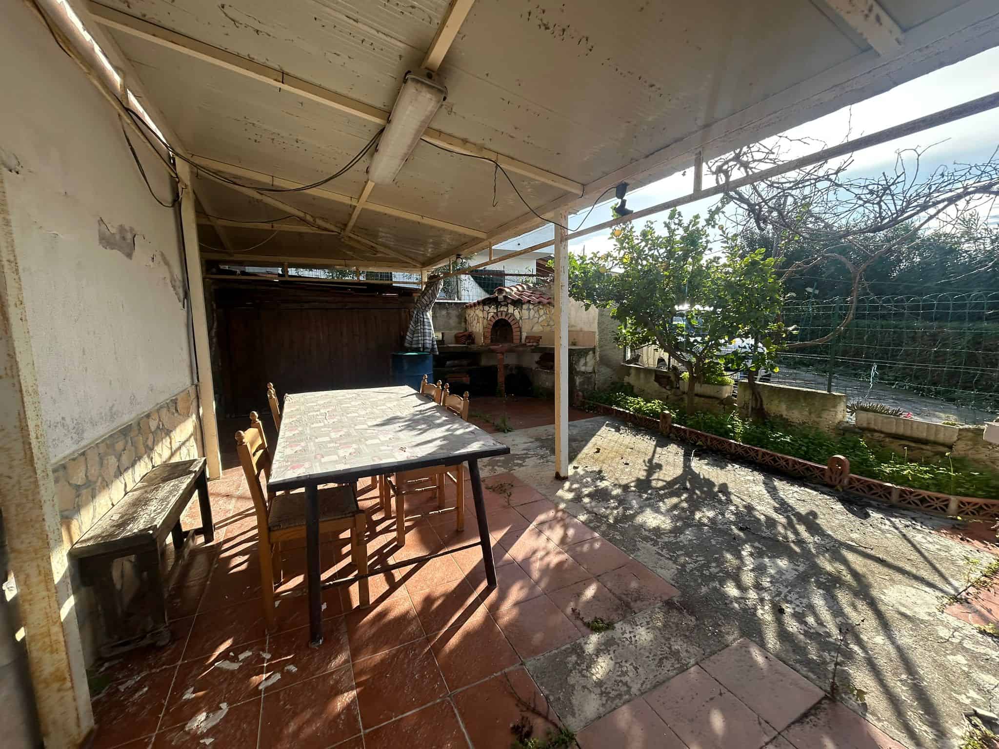 Vecchia veranda con area pranzo esterna e forno a legna, giardino con piante, ambiente rustico e accogliente, ideale per vivere il relax all'aperto in un'atmosfera tradizionale.
