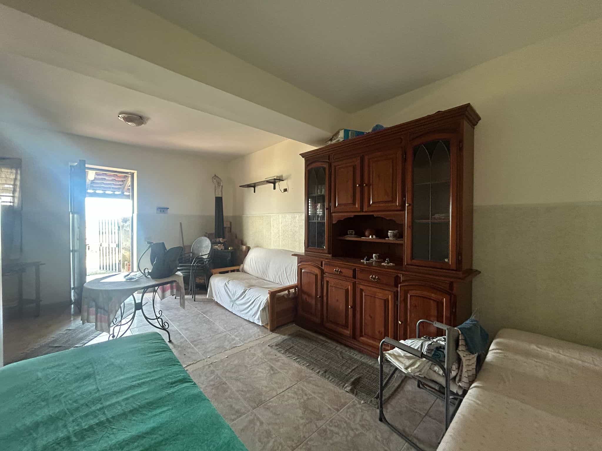 Divano in soggiorno con mobile in legno e lettini in una casa di campagna, ambiente accogliente con luce naturale, ideale per case di vacanza o status di vita rilassata.