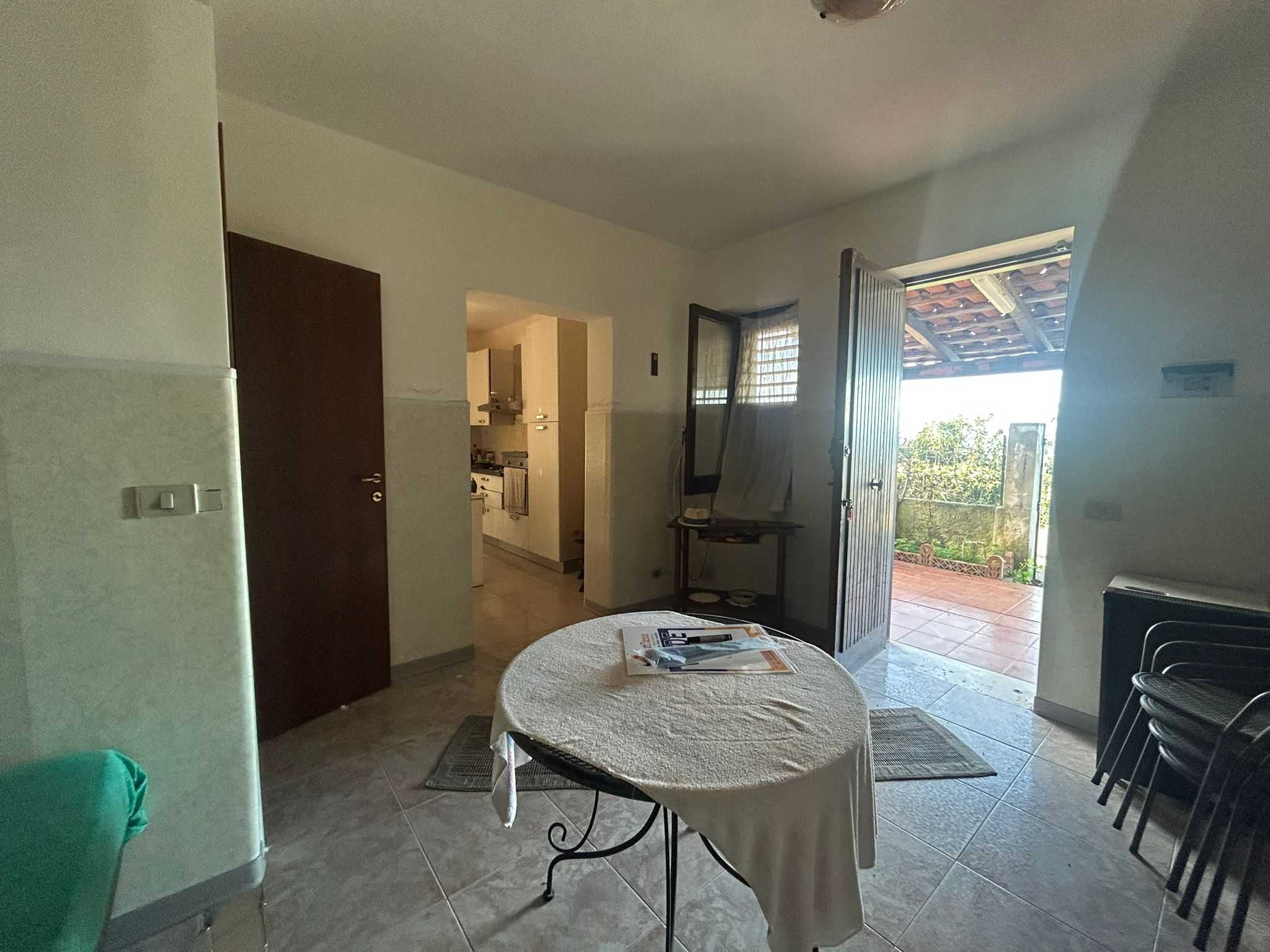 Interno del soggiorno di una casa con porte che conducono a una terrazza, cucina in vista, arredamento semplice e luminoso, ideale per le esigenze di famiglie o coppie in cerca di abitazioni accoglienti.