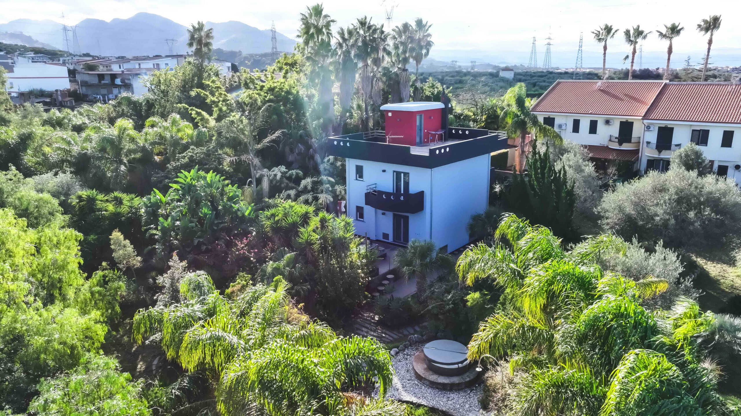 Casa moderna circondata da giardino tropicale con piante verdi e palme, vista panoramica sulle colline, ambiente tranquillo e rilassante, soluzione residenziale di lusso NextCasa.
