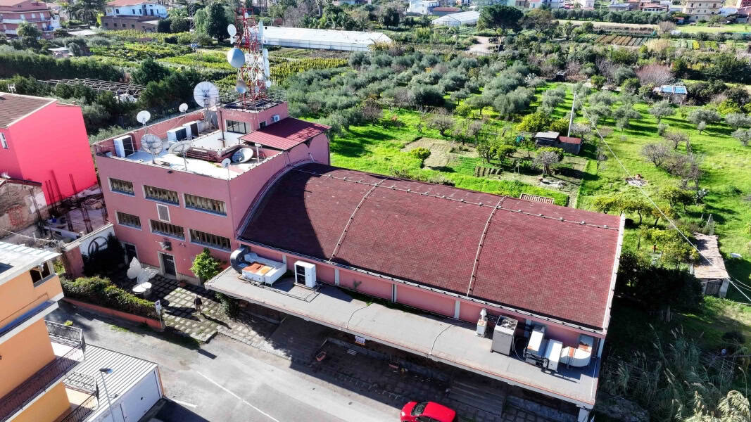 Tetto di edificio residenziale rosa con impianti di antenna e climatizzazione, vista aerea su giardino con alberi e campagna circostante, in zona rurale tranquilla, immobile in vendita.