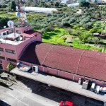 Tetto di edificio residenziale rosa con impianti di antenna e climatizzazione, vista aerea su giardino con alberi e campagna circostante, in zona rurale tranquilla, immobile in vendita.