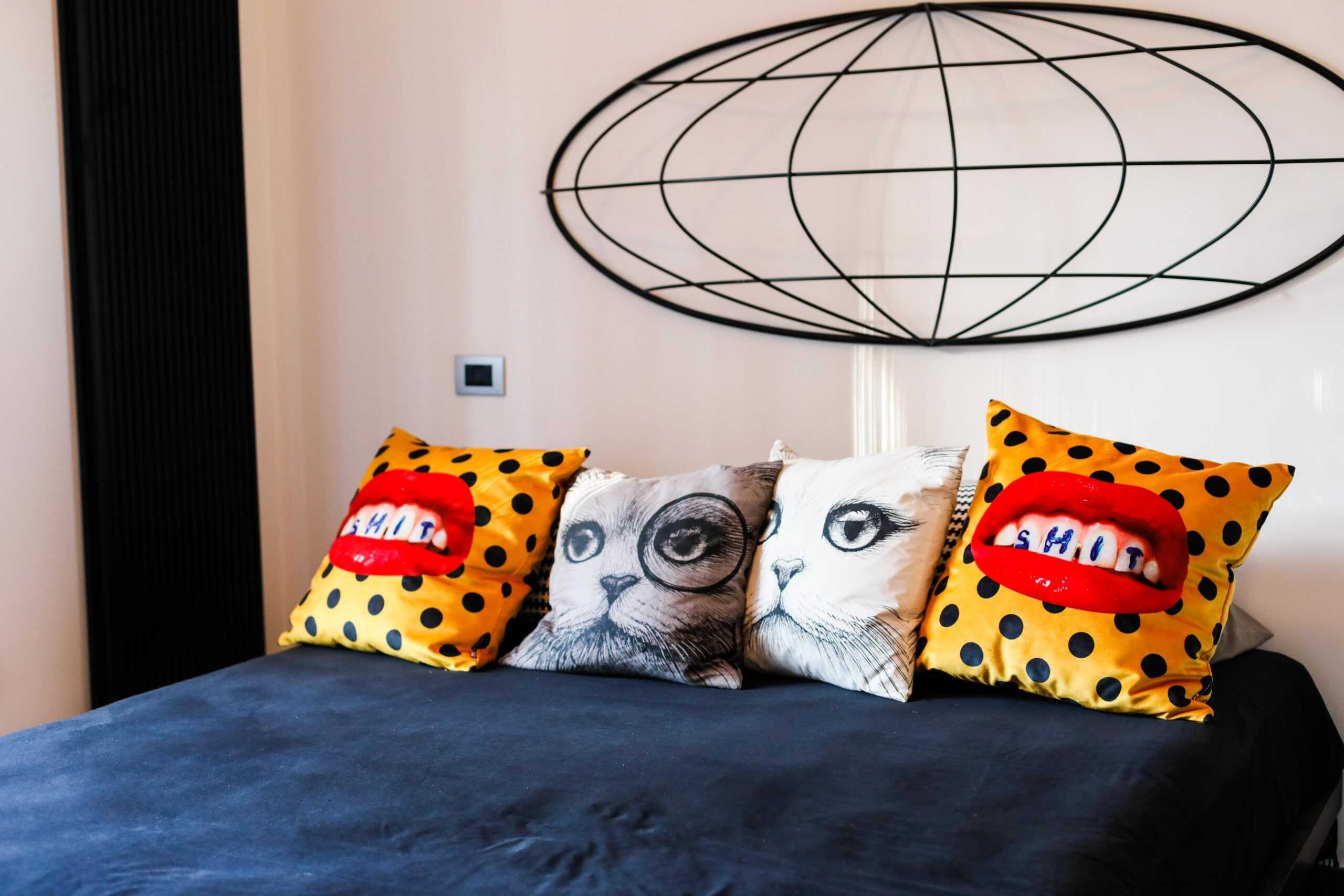 Diversi cuscini decorativi con stampe artistiche su letto matrimoniale in camera moderna, dettagli di arredo di stile contemporaneo, elementi di design colorati per ambienti casa accoglienti e alla moda.