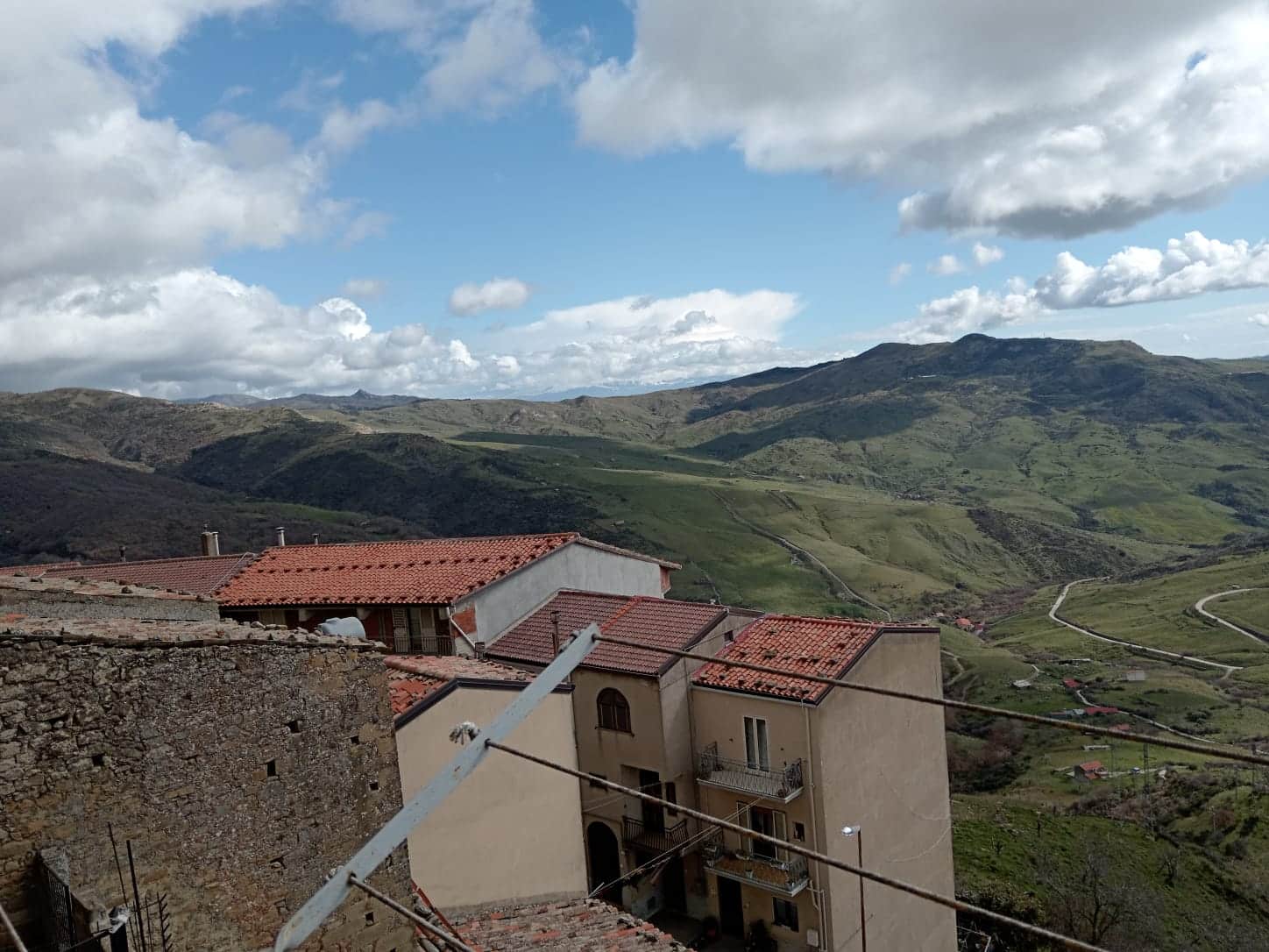 Casette con tetti rossi e vista panoramica sulle montagne verdi, cielo nuvoloso, paesaggio Toscano, ambientazione rurale e tranquilla, ideale per immagini immobiliari e scenari naturalistici.