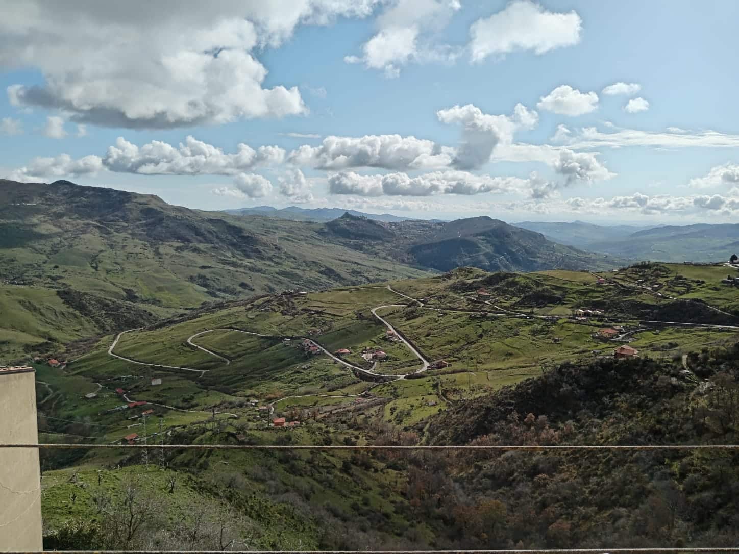 Panorama delle colline verdi e delle strade tortuose in un paesaggio rurale calabrese, con nuvole sparse nel cielo azzurro, ideale per immobili o proprietà immerse nella natura.