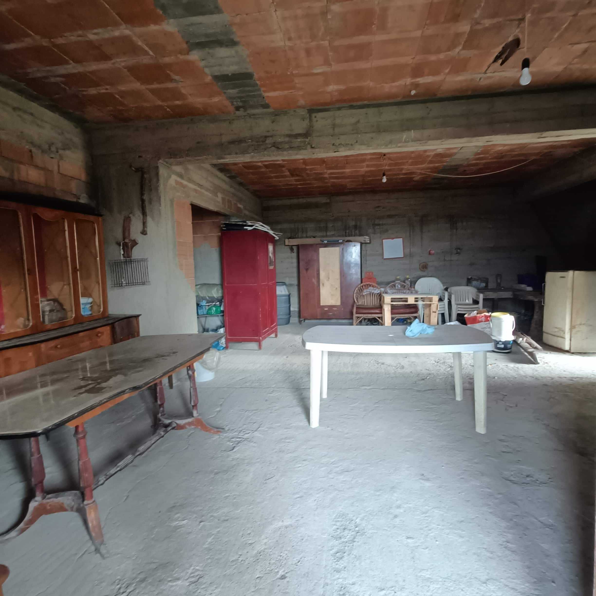 Appartamento in costruzione, spazio interno con muri in cemento e intonaco grezzo, presenza di mobili temporanei e materiali da edilizia, pronto per ristrutturazione totale.