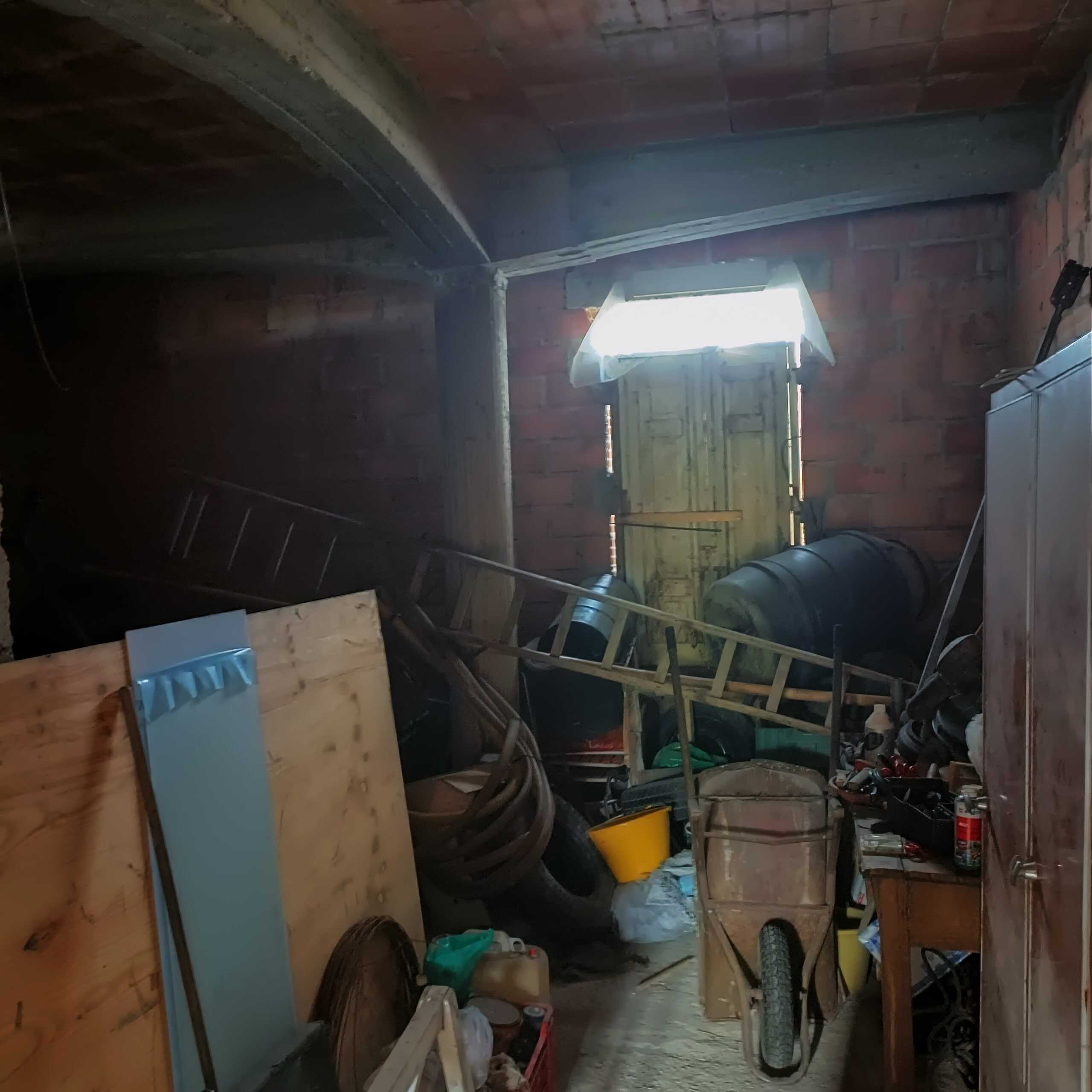 Vecchia soffitta in muratura con attrezzi da fai da te, scatole e materiali per ristrutturazione, luce naturale attraverso finestra, spazio di deposito, ambientazione rustica e immersa nel bricolage.