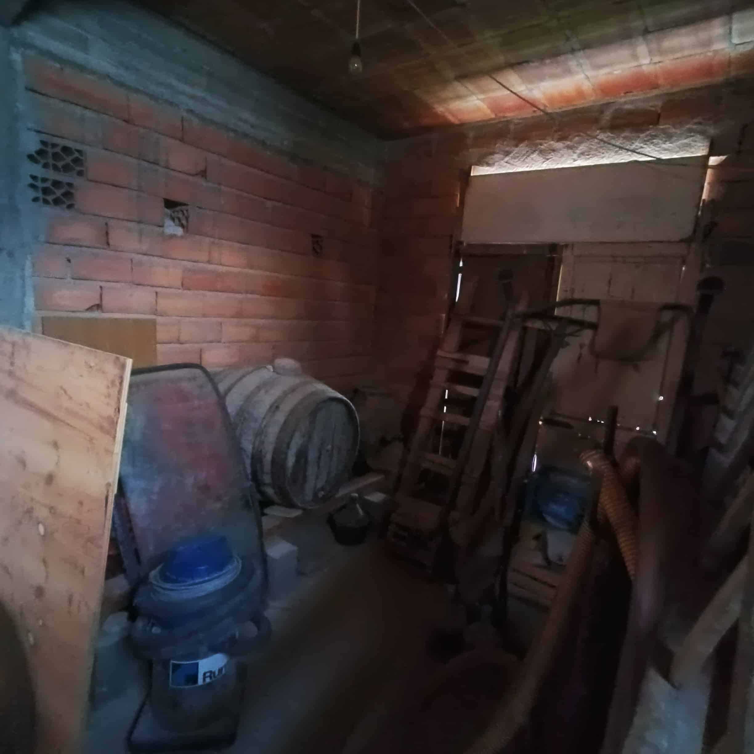 Magazzino in costruzione con mattoni a vista, accessori da lavoro, botte in ferro, scala e tubature, spazio di stoccaggio per ristrutturazioni o materiali edilizi.