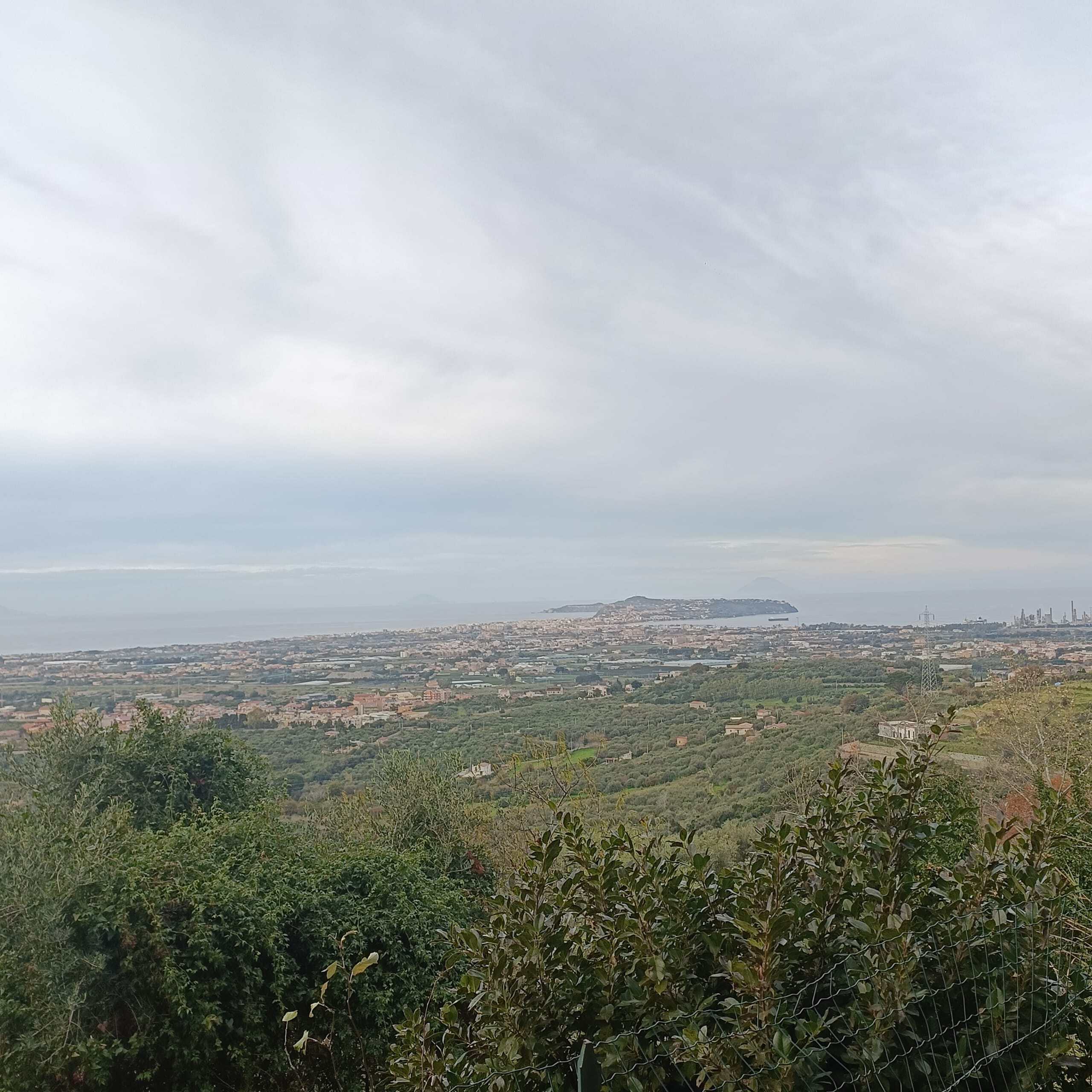 Panorama di un paesaggio naturale con vista sulla città e il mare, ricco di vegetazione, colline e cielo nuvoloso, ideale per immobili eco-sostenibili e immobili con viste panoramiche, immobili in zone verdi.